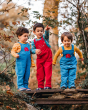 Three children exploring outside and stood on a stone bridge, with two children wearing the Frugi x Babipur natural organic cotton cord Blue Dungarees, and the child in the middle wearing the red Frugi x Babipur Dungarees. All have a red elephant patch on