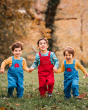 Three children running in a grassy field with trees in the background. Wearing the Blue Frugi x Babipur Natural Organic Cotton Cord dungarees, with the child in the middle wearing the Red Frugi x Babipur dungarees