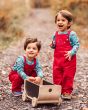 Two children playing on a leafy path with a toy cart, both of them wearing the Frugi x Babipur natural organic cord dungarees in Red