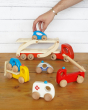 Hand reaching down to play with the Bajo handmade wooden transporter lorry and emergency vehicle toys on a wooden table