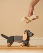Hand holding a Bajo wooden dachshund puppy toy above a Bajo pull along dachshund on a wooden floor