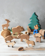 Bajo Wild Animals Forest Set, Wooden forest animal figures stacked on top of each other and include: Fox, Wolf, Bison, Squirrel, Deer, Hog, Owl, Raccoon, Bear, on a wooden surface with a Holztiger tree in the background. 