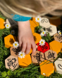 Close up of a child's hand playing with the Bajo wooden hive block toys next to some white flowers