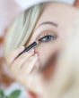 A person doing their make-up in a mirror using the Green People Carbon Black Eye Liner Pencil