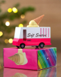 Candylab pink and white toy ice cream truck on top of its cardboard box in front of some Christmas lights