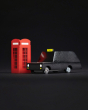 Close up of the Candylab black London taxi toy on a black background next to a miniature red phonebox