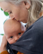 Close up of woman kissing the head of a baby in the close caboo lite baby carrier in the nightfall colour