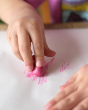 Close up of a child drawing with a pink Crayon Rock on some white paper