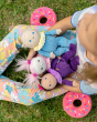 A child holding Freya Fondant, Bonnie Buttercream and Clara cupcake in the lap, sat on a grassy field