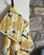 DUNS Sweden organic cotton linen pot holder and tea towel in the bee yellow print handing from a metal hook next to a stone wall 