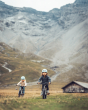 2 children riding Early Rider seeker kids bikes in front of a wooden hut and mountain