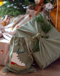 Close up of a Christmas present wrapped in the Fabelab eco-friendly reusable gift wrapping sheets, next to a pile of Christmas presents and an embroidered drawstring bag