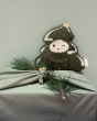 Fabelab kids organic cotton cuddly Christmas tree toy on top of a green Christmas present with a small branch of a Christmas tree