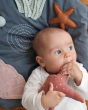 Close up of a baby laying on the Fabelab underwater soft activity blanket, holding a soft starfish toy to its mouth