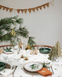 Close up of a white and green Christmas dinner table with a Fabelab festive Christmas garland hanging on a wall in the background