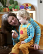 An adult and child happily sat together, with the child wearing the Frugi x Babipur natural organic cotton dungarees with a red elephant on the front chest pocket