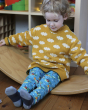 A child happily playing on a Wobbel Board whilst wearing a yellow jumper with clouds and the Frugi x Babipur Word Printed Libby Leggings in Natural Organic Cotton