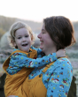 An adult carrying a child, both are smiling and both are wearing the Frugi x Babipur World printed Bryher top for kids and adults