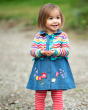 Young girl stood on some gravel wearing the Frugi embroidered floral emma chambray dress