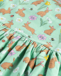 A closer view of the playful Spring Time print on the Frugi GOTS Organic Cotton Morwenna Skater Dress - Riverine Rabbits. The print of the dress shows light brown rabbits, yellow, white and pink flowers, bee and lady birds along with the pleated section o