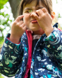 Close up of a girl holding a flower in front of her eye wearing the Frugi eco-friendly pegasus print rain coat