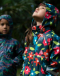 Close up of two young children stood wearing the Frugi eco-friendly rainy days waterproof jackets with the hoods up 