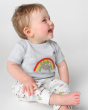 A happy toddler sat down and wearing the Frugi Children's GOTS Organic Cotton Frankie Summer Outfit - Sleepy Sloths. A beautiful 2 piece outfit including a grey short sleeved top with a sloth and rainbow character applique with comfy white cuffed sloth an