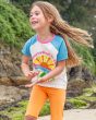 A child happily playing on a beach, with rocks and trees in the background. The child is wearing a Frugi Conservation Top and the Orange Laurie Shorts 2 Pack in Orange Blossom/Tangerine 