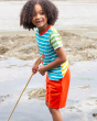 A child smiling and playing on the beach with a long stick. The child is wearing Frugi Switch Samson Shorts - Orangutan and the Frugi Hotchpotch Applique T-shirt in Lobster.