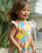 A child smiling and happily outside, wearing the Frugi Children's Organic Cotton Etta Play-suit - Patchwork. A bright and colourful patchwork play-suit with beautiful flower print in patchwork squares.