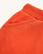 A close up view of the pockets, stitching and waistband on the Frugi Switch Samson Shorts - Orangutan. Orange organic cotton brushback shorts with functional blue drawstring elasticated waistband and pockets, made from GOTS In-Conversion Cotton, on a crea