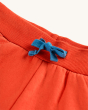 The blue drawstring and orange waistband of the Frugi Switch Samson Shorts - Orangutan. Orange organic cotton brushback shorts with functional blue drawstring, elasticated waistband and pockets, made from GOTS In-Conversion Cotton, on a cream background.