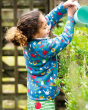 Close up of young girl tipping water over a plant, wearing the Frugi national trust garden print snuggle fleece