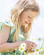 A child happily playing in the sun and picking flowers, wearing the Frugi Morwenna Skater Dress - Riverine Rabbits