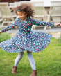 Young girl spinning round on some grass wearing the Frugi blue floral print sophia skater dress