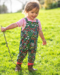 Young girl walking on some grass wearing the Frugi floral print parsnip dungarees