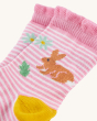 A closer view of the pink and white frilled socks. On the socks is a light brown rabbit, mint green coloured flower, and a green leaf. On a cream background
