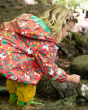Young girl bending over to fill a jug of water in a river, wearing the Frugi eco-friendly pegasus print puddle buster jacket