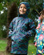 Young child stood under some trees wearing the Frugi rainbow ramble rainy days jacket with the hood up