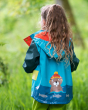 Young girl stood in some long grass wearing the Frugi beaver print puddle buster raincoat