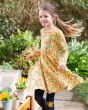 Young girl stood in a garden wearing the Frugi yellow floral print skater dress