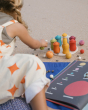 A child playing on the beach with the Grapat Dear Universe Wooden Play Set. The child is carefully placing the planets around a wooden board filled with colourful, rainbow pots