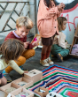 Children crouched down on a rainbow striped blanket around the Grapat plastic-free wooden permanence box