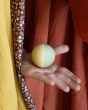 A green and yellow ball from the Grapat Moonlight Tale Play Set being held on an open palm, on a colourful fabric background