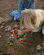 A child sat on the beach gathering various Grapat Rainbow Mandala pieces into their hands