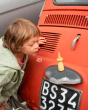 Close up of young boy leaning down to look at a plastic-free Grapat nini toy figure on the back of a red car