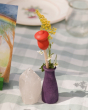 The purple vase from the Grapat Your Day Wooden Celebration Set holds yellow and white flowers, a read wooden flower, and is stood next to a shiny, white crystal