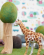 Close up of a green rubber toys giraffe figure on some green felt next to a papoose wooden tree toy