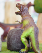 Close up of a green rubber toys t-rex stood on some green felt in front of a papoose felt rock toy
