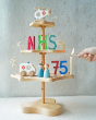 A Grimm's seasonal festivity stand decorated to celebrate the NHS's 75th birthday. The decorations Include a Bajo helicopter and ambulance, Grimm's Anthroposophical letters and numbers and two Peepul peg doll figures, a doctor and nurse.